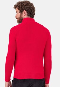 Pull rouge en maille avec un col montant, des manches longues, des poignets et un ourlet côtelés. Texture lisse, silhouette ajustée, détails de couture visibles.