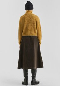 Khaki corduroy midi-rok gecombineerd met een mosterdgele fuzzy trui en een zwarte gebreide muts. Zwarte laarzen tot de knie maken de outfit compleet.