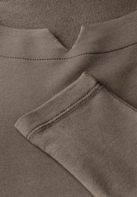 Tessuto di maglione marrone con design a V, caratterizzato da una texture liscia e dettagli di cucitura fine. Include un primo piano della manica piegata.
