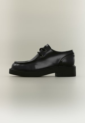 Chaussure de ville en cuir noir à lacets, bout carré arrondi et petit talon bloc, vue de profil sur un fond neutre.