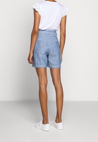 Chino kraťasy v světle modré lněné směsi, s vysokým pasem a ohrnutými lemy. Stylizované s bílou košilí a bílými teniskami.