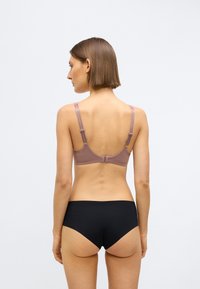 Šviesiai violetinės spalvos liemenėlė su reguliuojamais dirželiais ir užsegimu kabliukais, derinama su juodais šortais. Lygi tekstūra, paprastas dizainas, be matomų raštų.