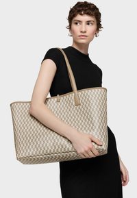 Bolso tote tejido en beige con un patrón geométrico, que cuenta con asas y detalles en cuero color marrón claro. Diseño espacioso con base plana para mayor estabilidad.