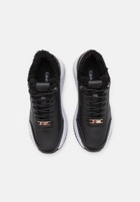 Svarta lädersneakers med faux fur-fodring, vit sula och guldförsedda snören. De har en strukturerad design för grepp och komfort.