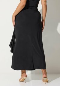 Gonna maxi nera con texture liscia, leggero drappeggio e uno spacco alto. Abbinata a tacchi a stiletto nudi per un look elegante.