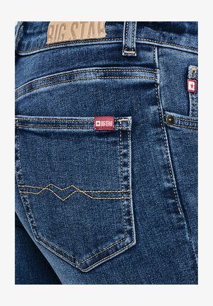 Sinine teksade tagatasku kollaste õmblustega ja punase sildiga, millel on kiri "BIG STAR".