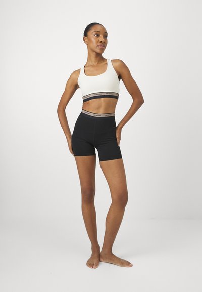 Pantaloni sportivi neri con vita alta, abbinati a un reggiseno sportivo crema con una fascia elastica grigia. Tessuto liscio, design aderente.