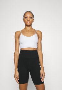 Top corto de canalé blanco con tirantes finos, combinado con pantalones cortos de ciclismo de punto negros de cintura alta, que cuentan con una cinturilla texturizada y un diseño ajustado.