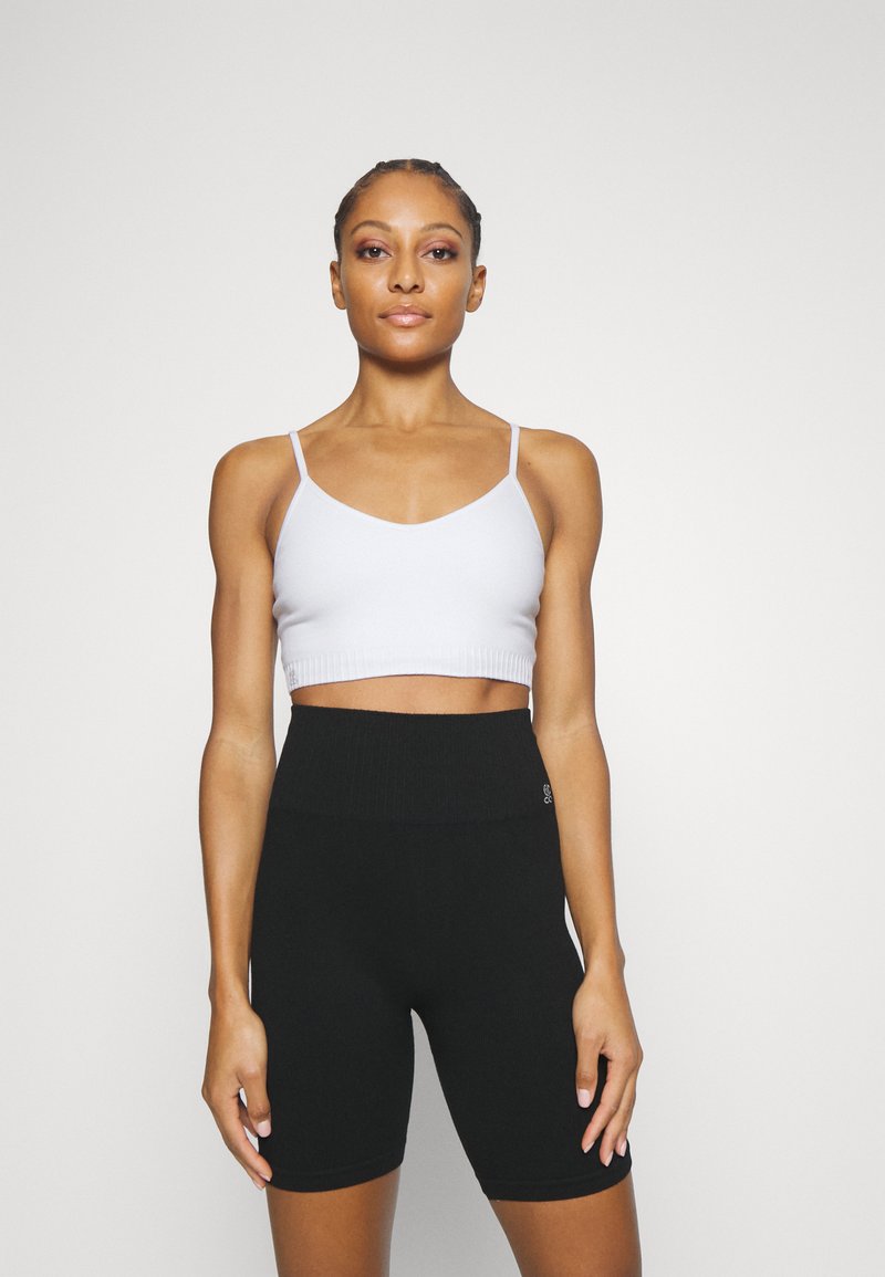 Top corto de canalé blanco con tirantes finos, combinado con pantalones cortos de ciclismo de punto negros de cintura alta, que cuentan con una cinturilla texturizada y un diseño ajustado.