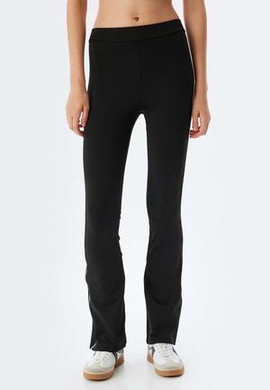 Zwarte leggings van rekbare stof, met een aansluitend ontwerp en een brede tailleband, gecombineerd met witte sneakers.