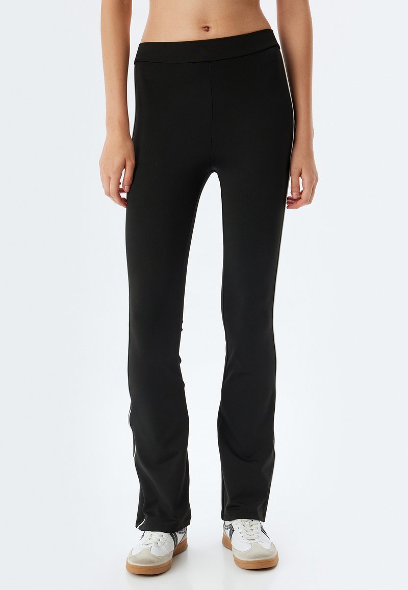 Leggings neri realizzati in un tessuto elastico, con un design aderente e una cintura larga, abbinati a scarpe da ginnastica bianche.