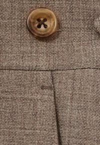 Tissu texturé marron avec un bouton rond proéminent présentant un motif en croix au centre et une petite poche fendue en dessous.