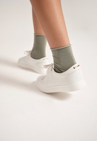 Białe skórzane sneakersy o teksturowanej powierzchni, z wiązaniem i złotymi akcentami. Połączone z oliwkowymi, bawełnianymi skarpetkami sięgającymi do połowy łydki.