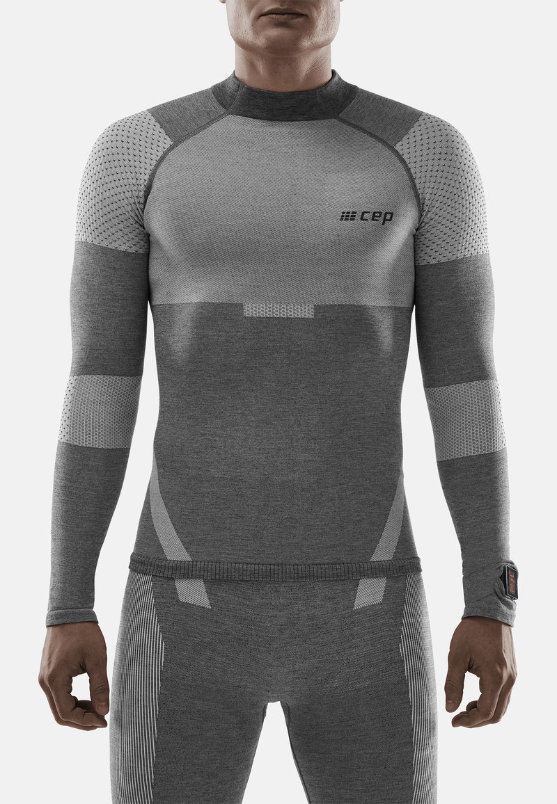Maglietta a maniche lunghe grigia in compressione con pannelli testurizzati e traspiranti. Presenta strisce sottili, un design aderente e un piccolo logo sul petto.