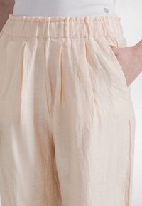 Lyse ferskenfarvede linnedbukser med elastisk talje, der har sidelommer og blødt, tekstureret stof med subtile folder.