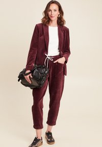 Bordeauxfarbener Cord-Anzug mit einem weißen T-Shirt und einer schwarzen Tasche. Die Schuhe haben ein Leopardenmuster. Lässige, entspannte Passform mit sichtbaren Taschendetails.