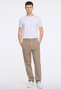 Beige chino's met voorplooien, gecombineerd met een eenvoudig wit t-shirt. Witte sneakers maken de outfit compleet, met een eenvoudig, klassiek ontwerp.