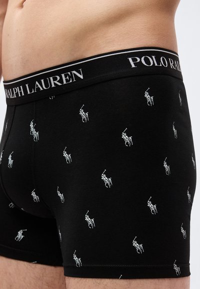 Αρσενικός κορμός που φοράει μαύρα μποξεράκια Polo Ralph Lauren με λευκά λογότυπα παίκτη πόλο και ζώνη με επωνυμία σε κοντινή πλάγια όψη.
