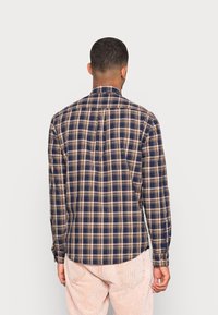 Camisa de cuadros en tonos azul marino y beige, hecha de algodón. Presenta mangas largas, un cuello y un dobladillo recto con detalle de pliegue en la parte posterior.