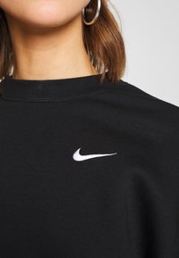 Svart sweatshirt i bomull med hög krage, prydd med en vit Nike-logotyp broderad på bröstet. Slen yta.