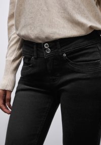 Mustat farkut korkealla vyötäröllä, joissa on kaksoispainonappi, etutaskut ja kontrastiväriset ompeleet. Pehmeä rakenne ja tiukka muotoilu.