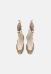 Beige ankelstøvler med en glat tekstur og en brun gummisål. Har elastiske sidepaneler og greb for nem påføring.