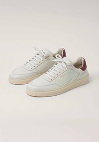 Bílé kožené tenisky s krémově bílou gumovou podrážkou, s bordó akcentem na patě, plochými tkaničkami a perforovanými detaily na špičce.