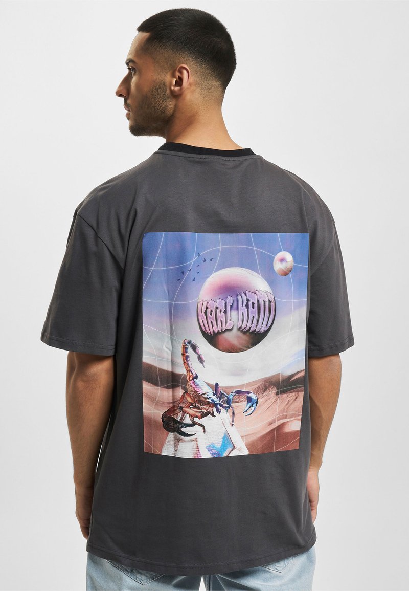 Gray oversized t-shirt featuring a large graphic on the back with a stylized scorpion, planet, and geometric grid design.