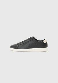 Zwarte leren sneaker met een gestructureerde afwerking, ronde neus, witte rubberen zool en een beige accent op de hiel. Voorzien van zwarte veters en logo-detail.