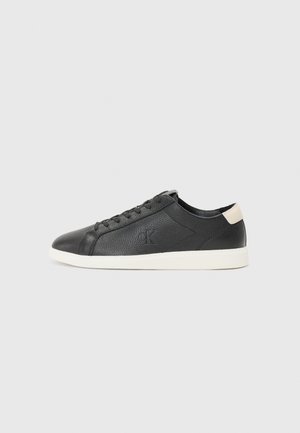 Sneaker in pelle nera con finitura texturizzata, punta rotonda, suola in gomma bianca e un accento beige sul tallone. Presenta lacci neri e dettaglio del logo.