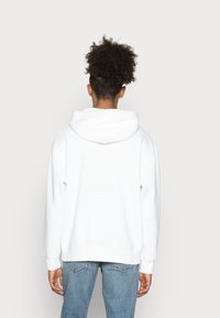 Sudadera blanca con capucha, hecha de material suave. Presenta un corte holgado, puños acanalados y un bolsillo tipo canguro. Diseño liso sin patrones.