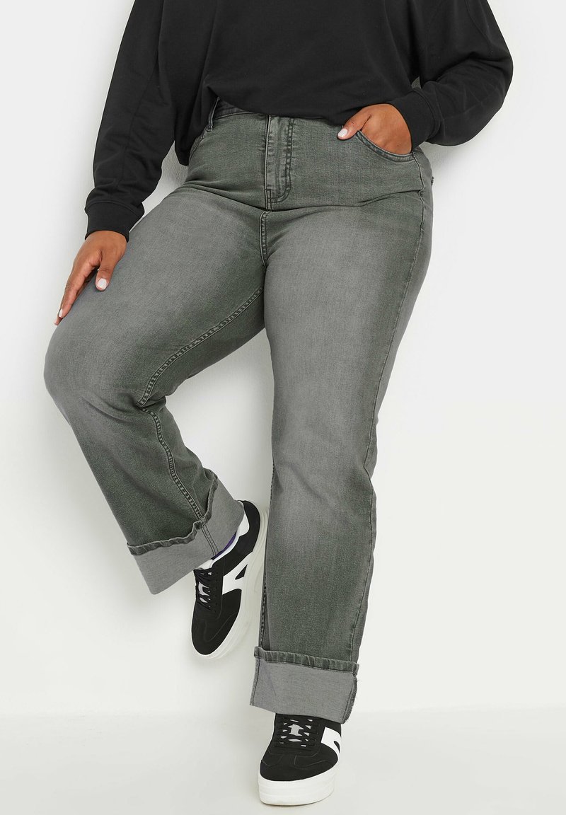 Jeans de mezclilla gris con un corte recto, dobladillos doblados y costuras simples. Combinados con zapatillas negras y blancas.