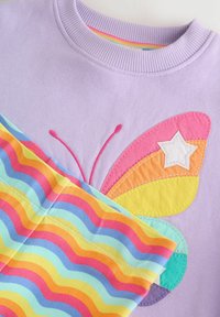 Ljubičasti pulover s dizajnom šarenog leptira s slojevitim krilima u ružičastoj, narančastoj i žutoj boji; u kombinaciji s tkaninom sa šarenim valovitim uzorkom u bojama duge.