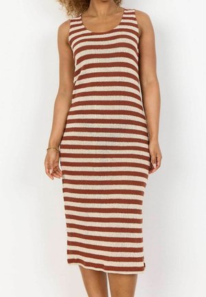 Frau trägt ein ärmelloses, knielanges Strickkleid mit horizontalen braunen und cremefarbenen Streifen, dazu eine dünne goldene Halskette und ein Armband.