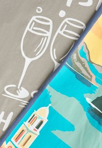 Δύο υφασμάτινα σχέδια διπλωμένα διαγώνια: το ένα με λευκά κτυπώντας ποτήρια κρασιού σε μπεζ, το άλλο με πολύχρωμο παράκτιο τοπίο και κτίριο.