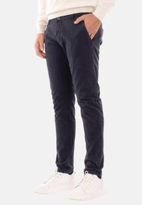 Pantaloni slim-fit in cotone morbido di colore blu navy, con tasche frontali e chiusura a un bottone, abbinati a sneakers bianche per un contrasto.