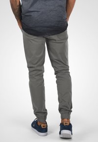 Gray jogger pants with elastic cuffs, side pockets, and a smooth texture, paired with blue suede sneakers featuring a logo accent.