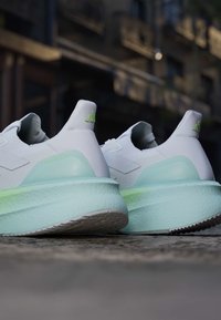 Chaussures de sport blanches et vert clair reposant sur une surface en pierre avec un arrière-plan urbain flou.