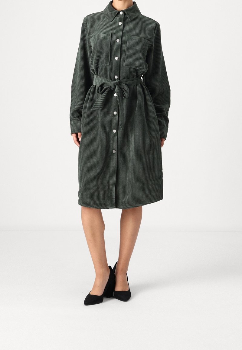 Robe chemise en velours côtelé vert foncé, avec un col, une fermeture à boutons sur le devant, deux poches poitrine et une taille ceinturée.
