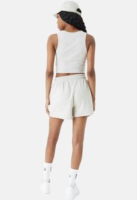 Helles graues, ärmelloses Cropped-Top und passende Shorts aus einem weichen Stoff. Ausgestattet mit einem elastischenBund. Weiße Socken und Sneakers runden den Look ab.