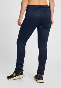 Marineblauwe sportbroek met een slim fit, elastische tailleband en zijzakken met rits, voorzien van een subtiele logodetail op het been. Zachte textuur.