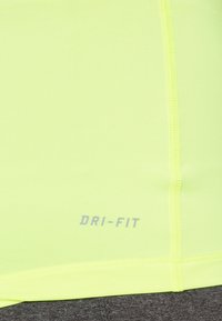 Tissu Dri-Fit jaune vif, texture lisse, avec un logo gris près du bas. Détail de couture visible le long des coutures.