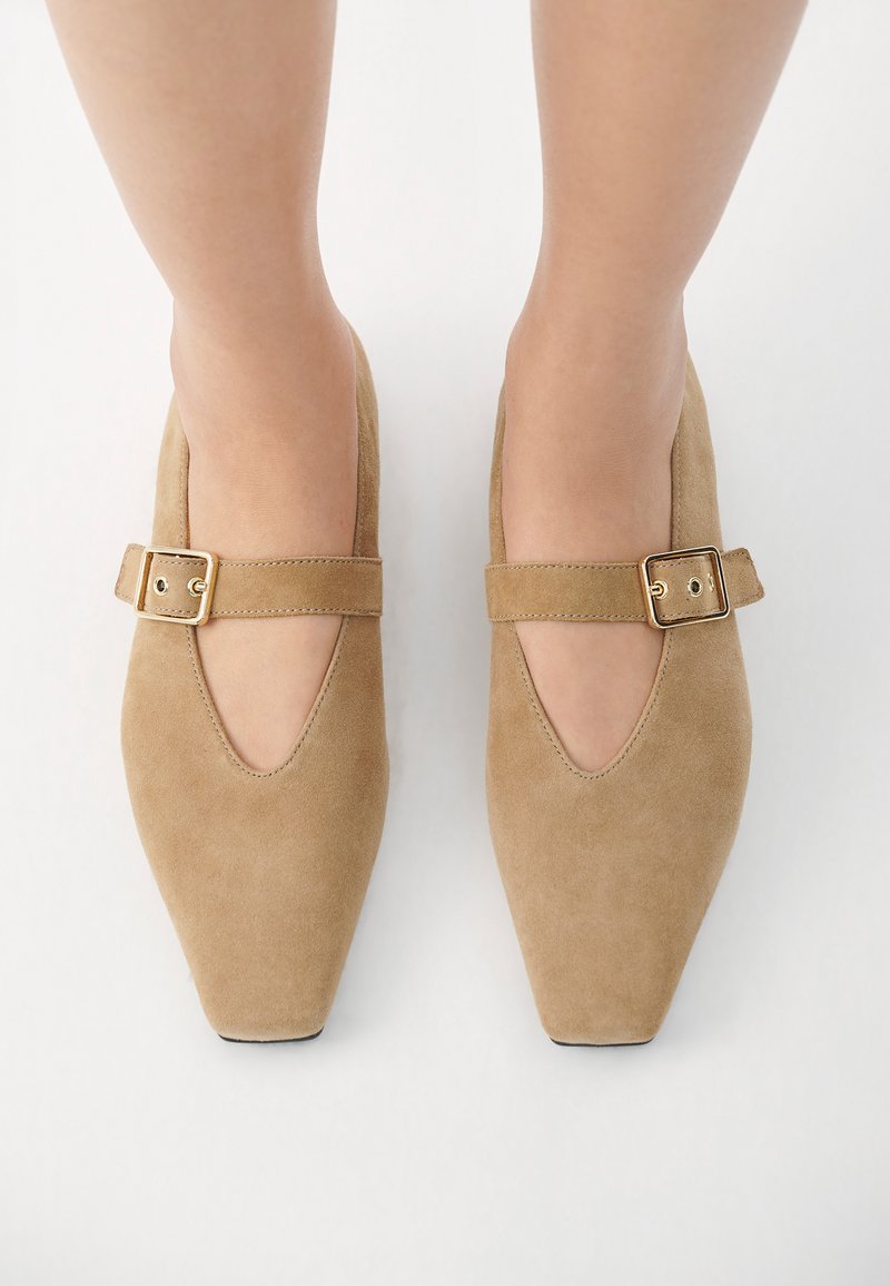 Jasnobrązowe zamszowe buty Mary Jane z zakładanym noskiem, z szerokim paskiem i prostokątną złotą klamrą. Gładka tekstura i elegancki design.