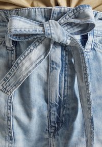 Světle modrá džínová sukně s mašlí v pase, vyrobená z texturované látky a s viditelnými švy podél okrajů.