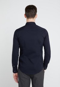 Mörkblå långärmad skjorta med en strukturerad krage, knapplåtsärmar och en slät tygfinish; figursydd design utan synliga mönster.