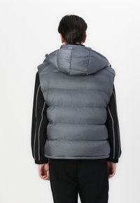 Grå polstret vest med hette, med en quiltet design og svarte sideakenter. Laget av et glatt, glinsende materiale.