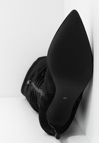 Black suede high-heeled boot with a pointed toe, gathered texture, and a side zipper. Size 37 marked on the sole.