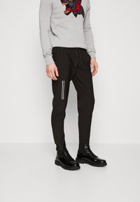 Svarta joggerbyxor med dragkedjeficka, elastisk midja och manchetter vid anklarna, kombinerat med en grå tröja med ett vargtryck.