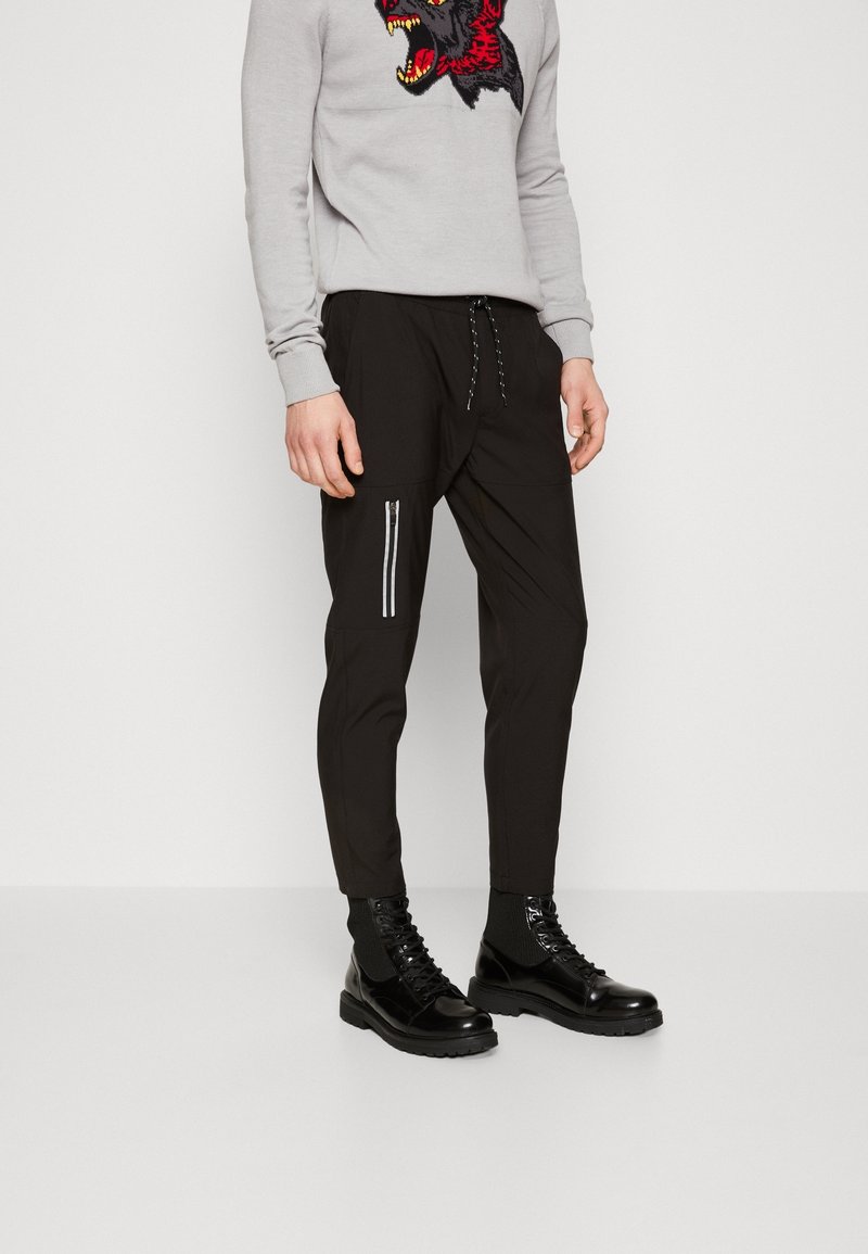 Svarta joggerbyxor med dragkedjeficka, elastisk midja och manchetter vid anklarna, kombinerat med en grå tröja med ett vargtryck.