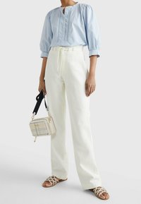 Blusa azul clara con mangas abullonadas y detalles de botones, combinada con pantalones de pierna ancha blancos, sandalias de tiras beige y un pequeño bolso de patrón de cuadros.